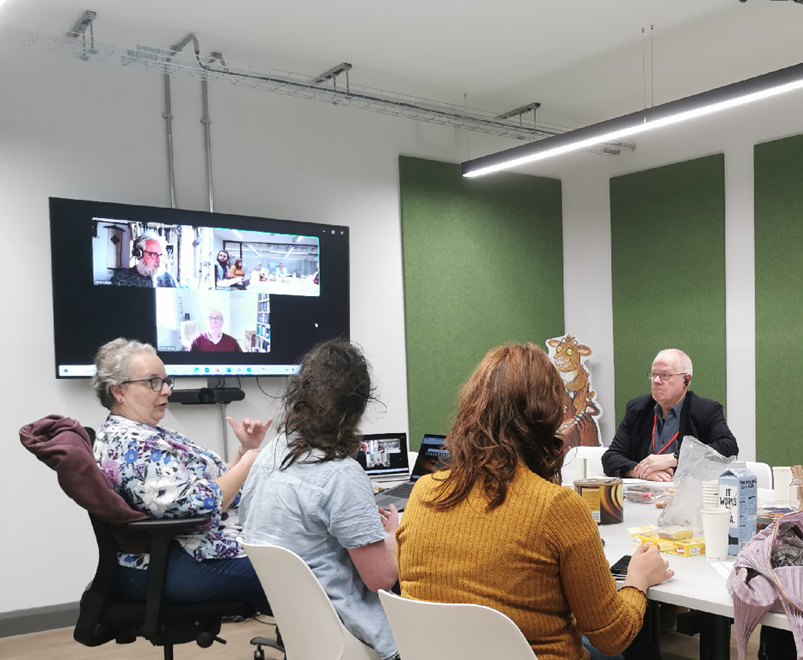 5 people sitting around a table with other participants on a video call   